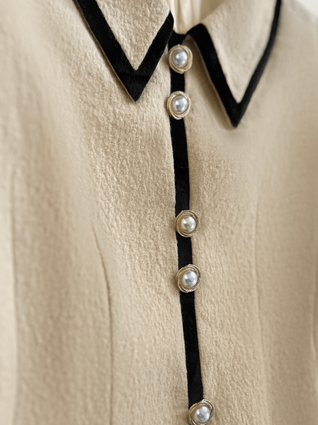 Close-up of a beige wool dress with black trim and pearl buttons.