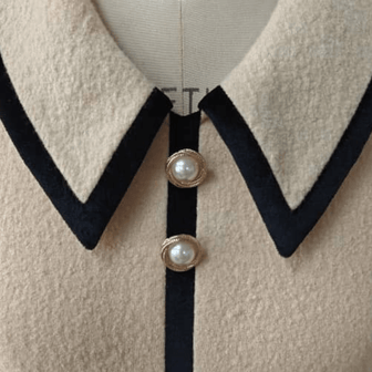 Close-up of a luxury ivory wool mini with black collar and pearl buttons on a mannequin.