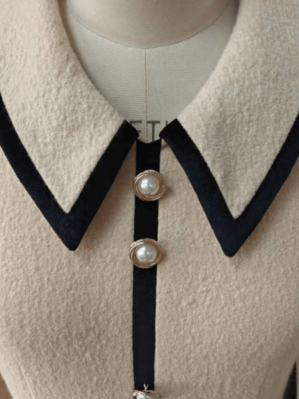 Close-up of a luxury ivory wool mini with black collar and pearl buttons on a mannequin.