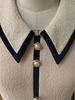 Close-up of a luxury ivory wool mini with black collar and pearl buttons on a mannequin.